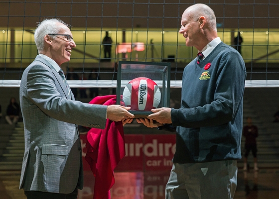 Larry Pearson accepting volleyball in glass box from President Vaccarino