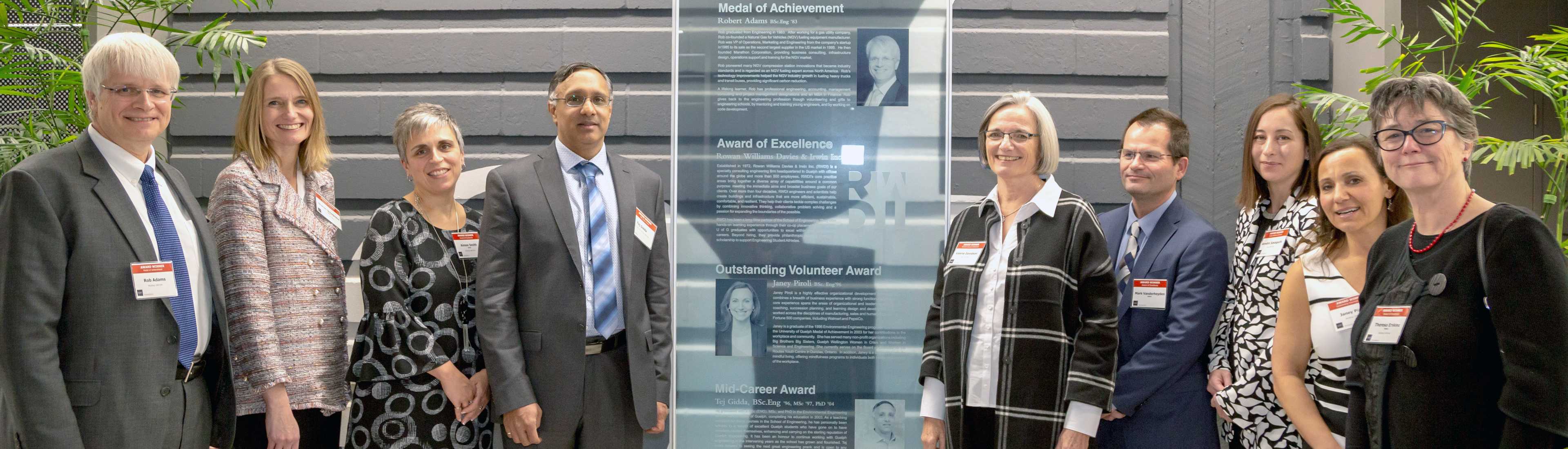 Group of individuals attending the School of Engineering Honours & Awards event, standing together in front of a recognition board, celebrating achievements in engineering. 