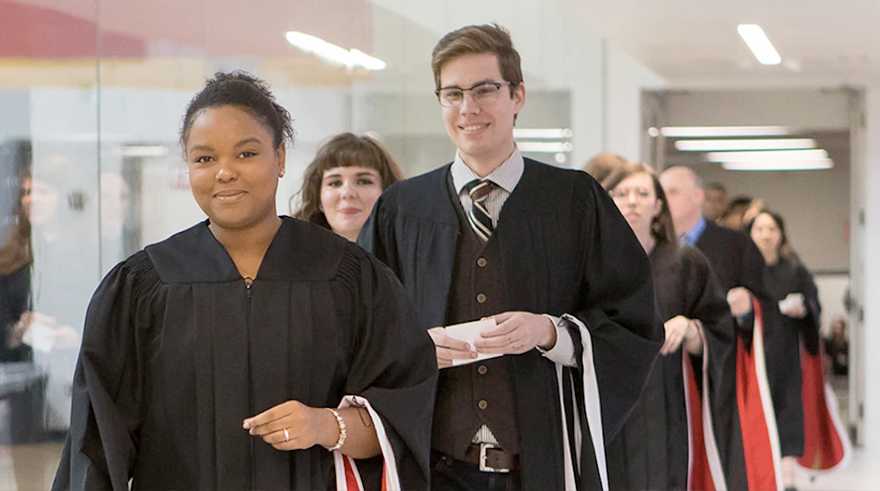 University of Guelph alumni walking in procession at a graduation ceremony, smiling and holding certificates.