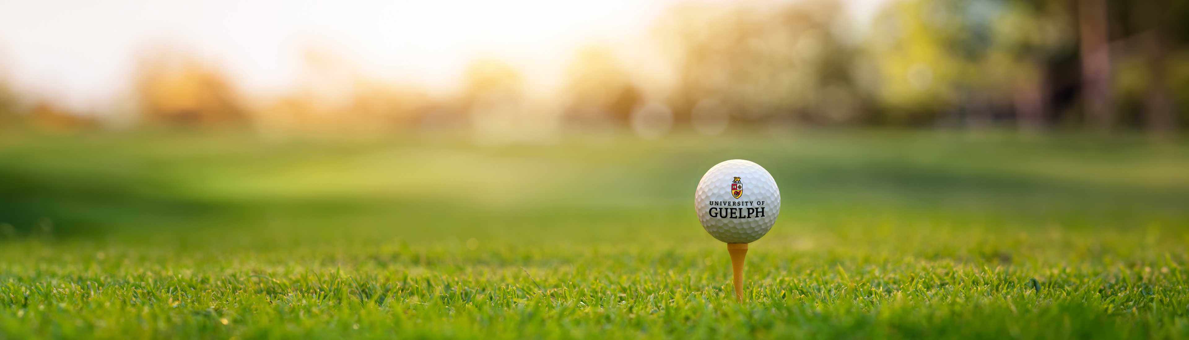 University of Guelph branded golf ball on a tee set against a blurred green background, promoting a university golf event. 