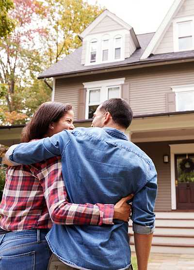 A couple embraces in front of a house.