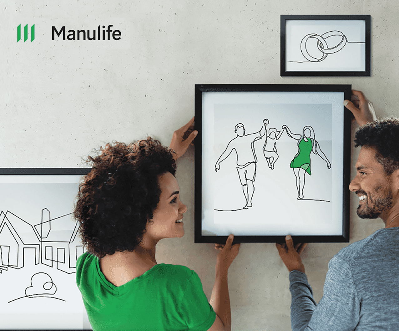 A couple hanging a framed minimalist line drawing of a family on a wall, smiling at each other, with a smaller framed drawing of wedding rings above.