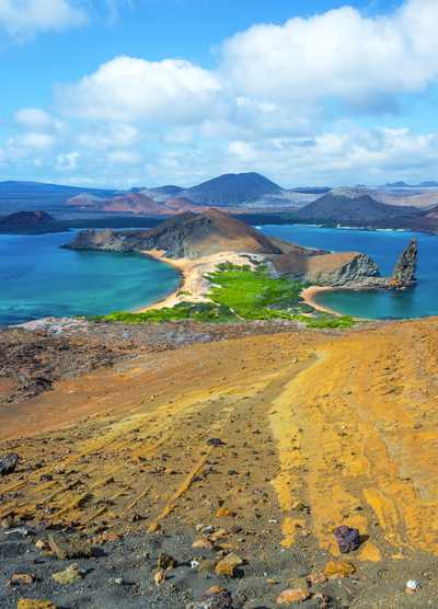 A breathtaking view from the top of Bartolome Island in the Galapagos, showcasing the volcanic landscape, turquoise waters, and the iconic Pinnacle Rock under a clear blue sky.