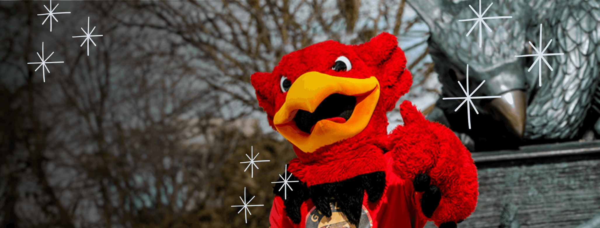 Grphon mascot posing in front of Gryphon statue in capus