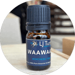 A bottle of LJ Turtle Aromatics Waawaa Northern Lights essential oil blend, featuring a dark blue label with a turtle logo, placed on a wooden surface with a blurred background.